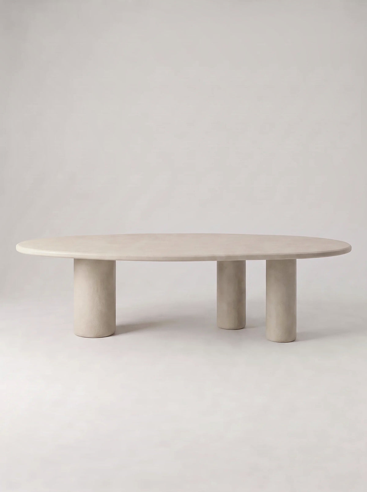 Steen eettafel met ovaal blad in beton ciré op drie ronde poten, vooraanzicht